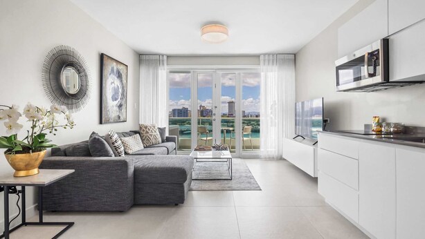 A modern apartment with a grey sofa, a coffee table, a dining table, and a kitchen area with a microwave. - Aqua Vista | Modern & Waterfront in Best Location (San Juan)