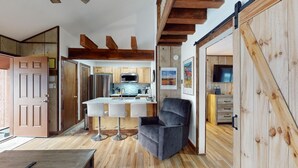 A modern kitchen with wooden beams, a bar area, and a grey sofa.