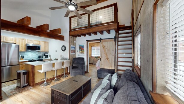 A spacious living area with a high ceiling, a kitchen with modern appliances, a dining area with bar stools, and a staircase leading to an upper level.