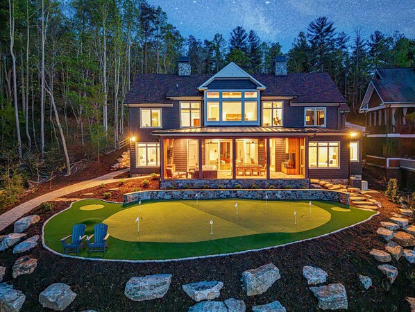 A two-story house with a large front porch, a well-maintained lawn, and a stone pathway leading to the entrance. - New Designer Lakefront Dock Putting Green Golf Sim (Nebo)