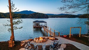A lakeside deck with a fire pit, seating, and a gazebo. - New Designer Lakefront Dock Putting Green Golf Sim (Nebo)