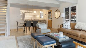 A modern living room with a brown sofa, a coffee table, and a dining area with chairs and a kitchen in the background.