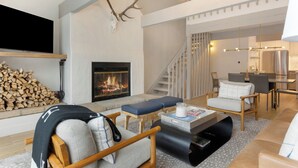 A modern living room with a fireplace, wooden furniture, and a staircase leading to an upper level.