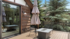 A wooden deck with a table and chairs, a glass door, and a large umbrella.