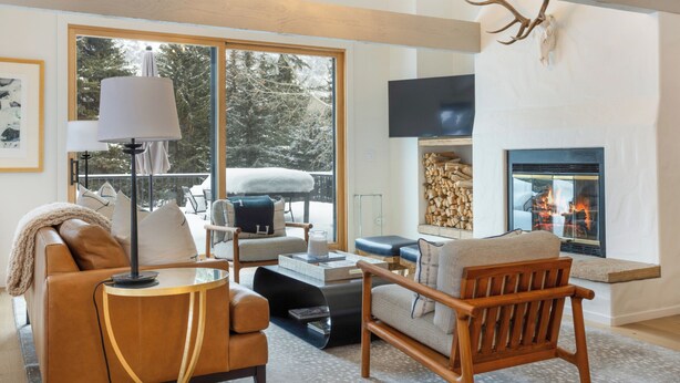 A cozy living room with a fireplace, comfortable seating, and a large window overlooking a snowy landscape.