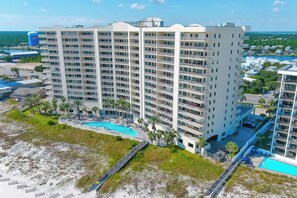 A multi-story hotel with a pool, surrounded by palm trees and a beach.