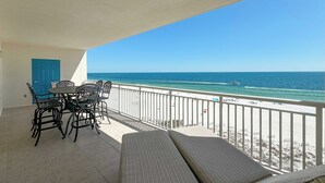 A balcony with a view of the beach and ocean, featuring a table and chairs, a blue door, and a white railing. - Admiral Quarters 705 | Beachfront | Indoor & Outdoor Pools | Beach Getaways (Orange Beach)
