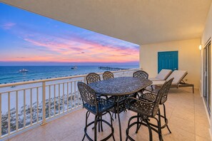 A balcony with a view of the ocean, a table with chairs, and a blue door. - Admiral Quarters 705 | Beachfront | Indoor & Outdoor Pools | Beach Getaways (Orange Beach)