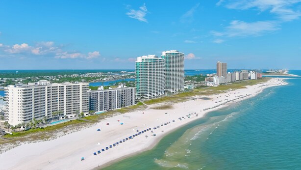 A coastal hotel with multiple high-rise buildings, a long beachfront, and a clear blue sky. - Admiral Quarters 705 | Beachfront | Indoor & Outdoor Pools | Beach Getaways (Orange Beach)