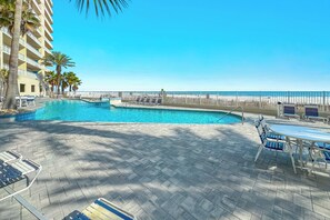 Zona de piscina de hotel con sillones de descanso, una mesa y vistas a la playa.