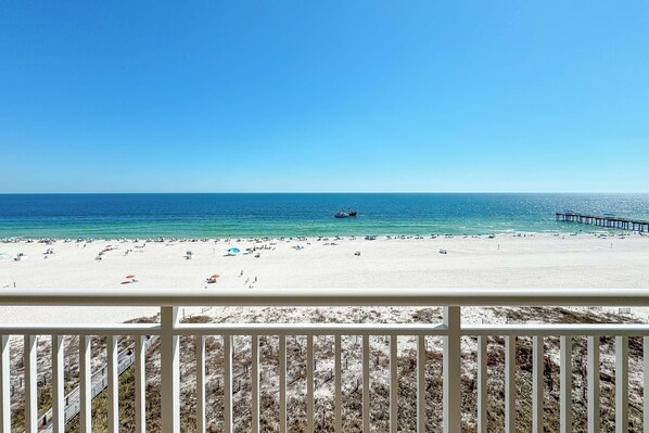 A beach with a pier extending into the water, sandy beach, and a clear blue sky.