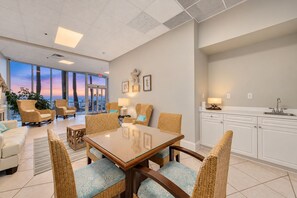 A modern hotel room with a dining area, a kitchen, and a view of the ocean. - Admiral Quarters 705 | Beachfront | Indoor & Outdoor Pools | Beach Getaways (Orange Beach)
