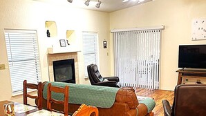 A living room with a fireplace, a television, a sofa, and a dining table with chairs. - Relax with the whole family or group of friends at this cozy Behr Hideout! (Alto)