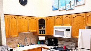 A kitchen with wooden cabinets, a microwave, stove, and a clock on the wall. - Relax with the whole family or group of friends at this cozy Behr Hideout! (Alto)