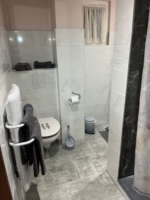 Une petite salle de bain équipée d’un WC, d’un sèche-mains, d’une poubelle et d’un porte-serviettes.