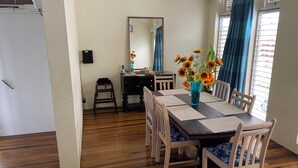 A dining area with a wooden table, chairs, a vase with flowers, a mirror, and a window with curtains. - Spacious 6-bedroom house in lovely Christ Church with WiFi, AC (Christ Church)