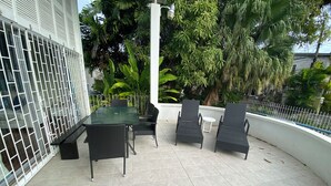 A patio with a glass-top table and four chairs, surrounded by a white fence and lush greenery. - Spacious 6-bedroom house in lovely Christ Church with WiFi, AC (Christ Church)
