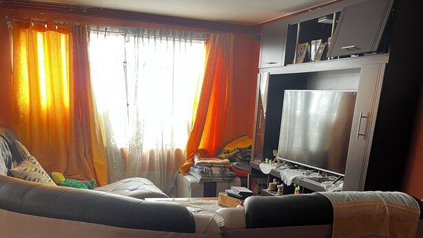 A living room with a curved sectional sofa, a television, and a kitchen area with a refrigerator and stove. - Beautiful house for rent in front of the Illimani in the city of La Paz.  (El Alto)