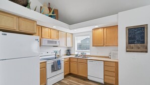 Een moderne keuken met houten kastjes, wit inbouwapparatuur en een prikbord met een welkomstboodschap.
