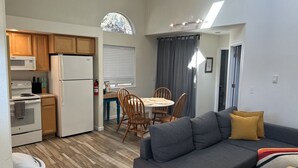 A compact living space with a kitchenette, dining area, and a gray sofa with yellow cushions.