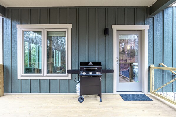 Un barbecue installé sur une terrasse en bois, avec vue sur une maison et des arbres.