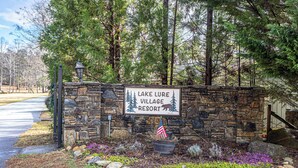 Un muro de piedra con un letrero del Lake Lure Village Resort, rodeado de árboles y un jardín ajardinado.