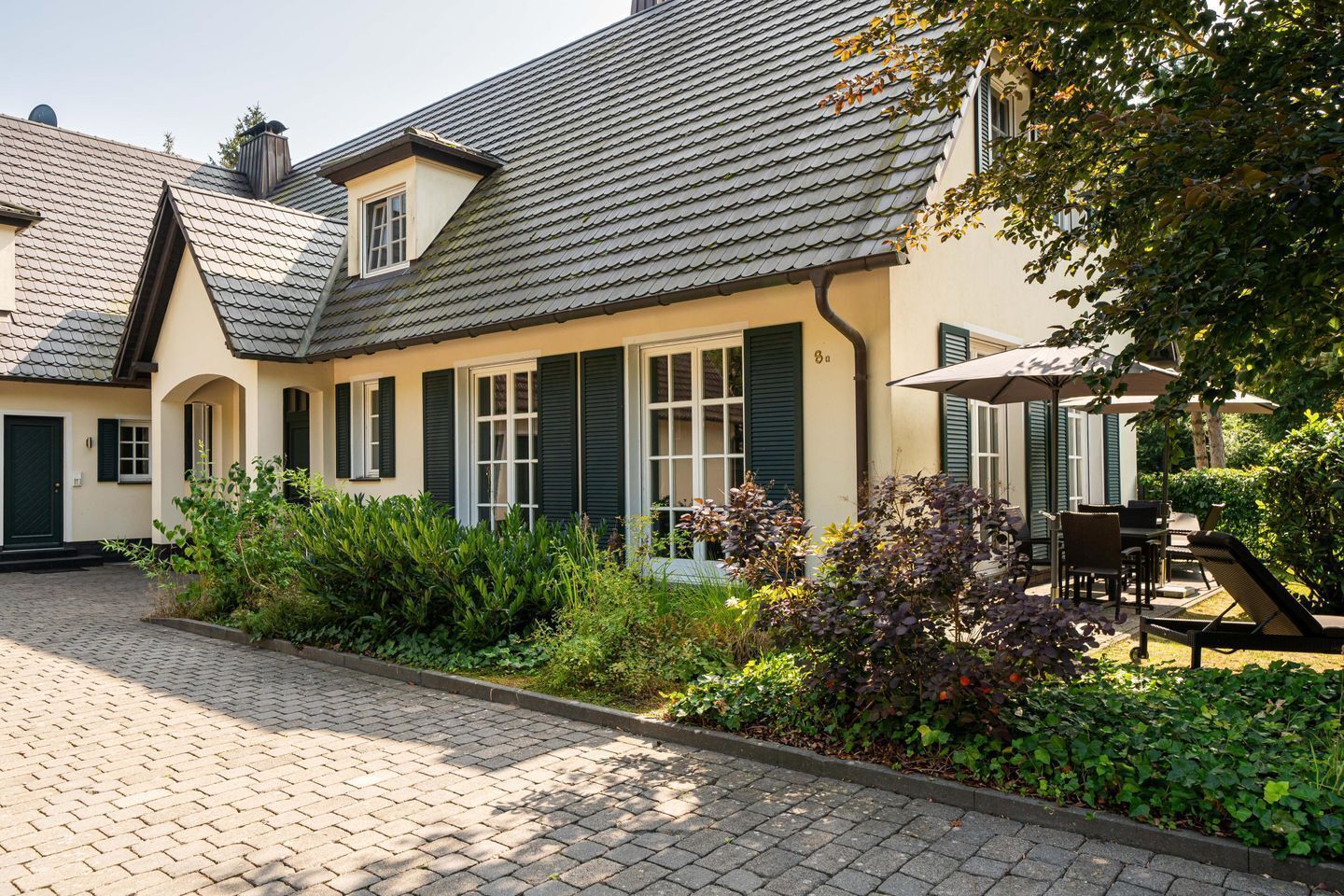 Una casa tradizionale con un cortile lastricato, persiane verdi e un giardino curato.