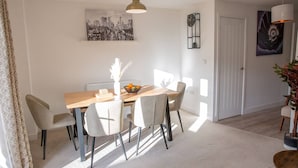 A dining area with a wooden table, white chairs, a vase with flowers, and a cityscape painting on the wall.