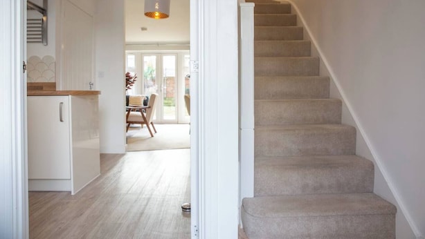 A staircase leading to a second floor, a kitchen area with white cabinets and a wooden countertop, and a dining area with a table and chairs.