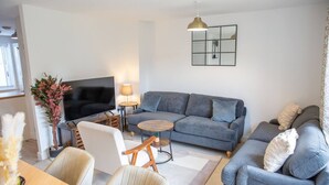 A modern living room with a grey sofa, a wooden coffee table, a TV, and a lamp.