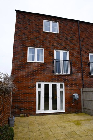 A two-story brick building with white-framed windows, a front door with glass panels, and a small garden area with a paved patio. - Bankside , cozy luxury home away from home. Spectacular home with free parking (Banbury)