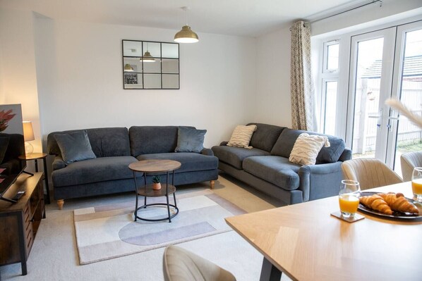 A modern living room with two sofas, a coffee table, and a dining table with breakfast items. - Bankside , cozy luxury home away from home. Spectacular home with free parking (Banbury)