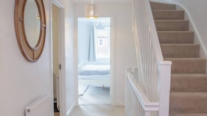 A hallway with a carpeted floor, a white radiator, a wooden-framed mirror, and a staircase with beige carpeted steps.