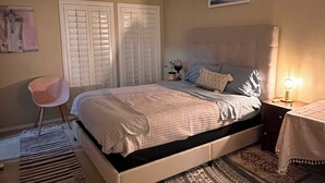 A bedroom with a bed, a ceiling fan, a nightstand with a lamp, a chair, and patterned rugs.