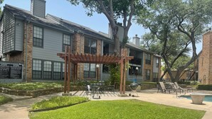 A courtyard with a pergola, outdoor seating, and a barbecue grill.