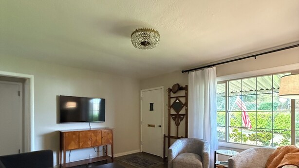 A living room with a flat-screen TV, a wooden cabinet, a sofa, a chair, and a large window with curtains. - The Garden Hideaway! East Medford, close to hospital, shopping and restaurants.  (Medford)