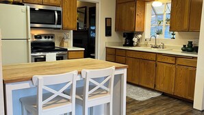 A kitchen with wooden cabinets, a white countertop, a built-in microwave, a stove, and a sink. There are two white chairs at a small table. - The Garden Hideaway! East Medford, close to hospital, shopping and restaurants.  (Medford)