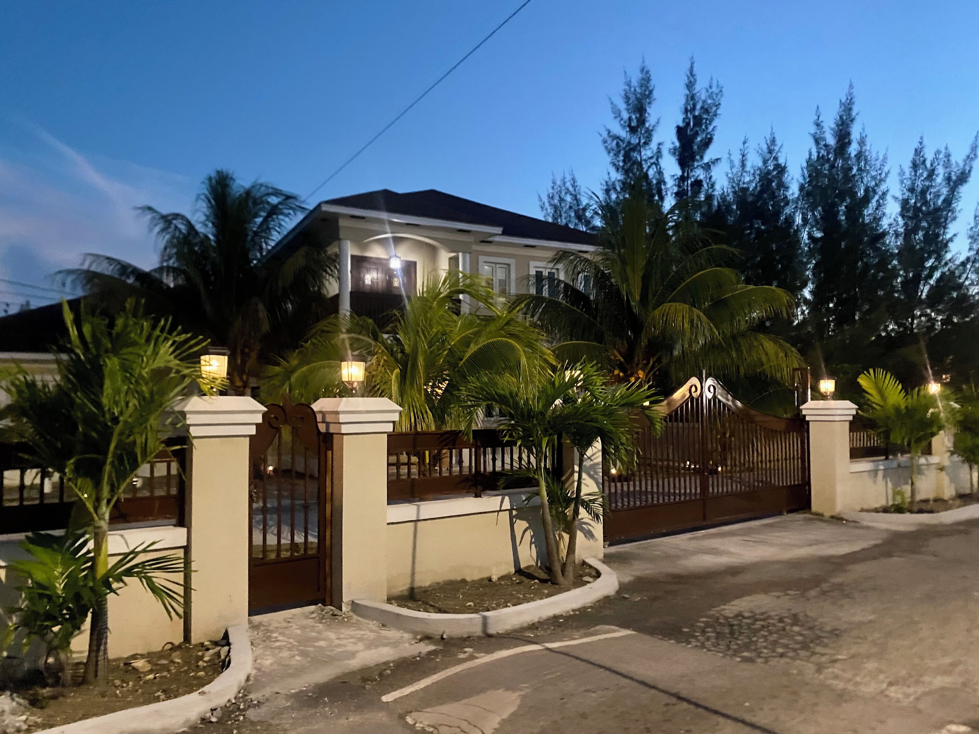 Propiedad residencial cerrada con una casa grande, palmeras y un césped bien cuidado.