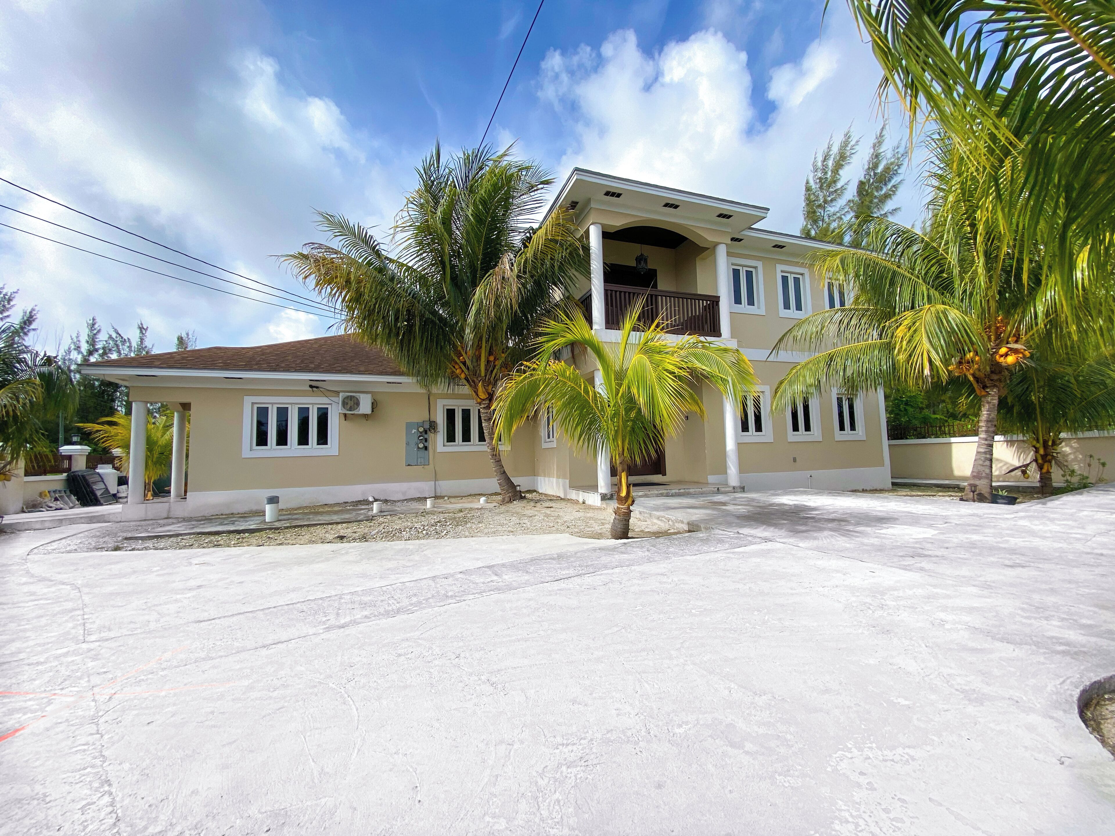 A two-story building with a balcony, surrounded by palm trees and a clear sky.