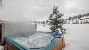 Una vasca idromassaggio in un ambiente esterno innevato, con un piccolo albero nelle vicinanze.