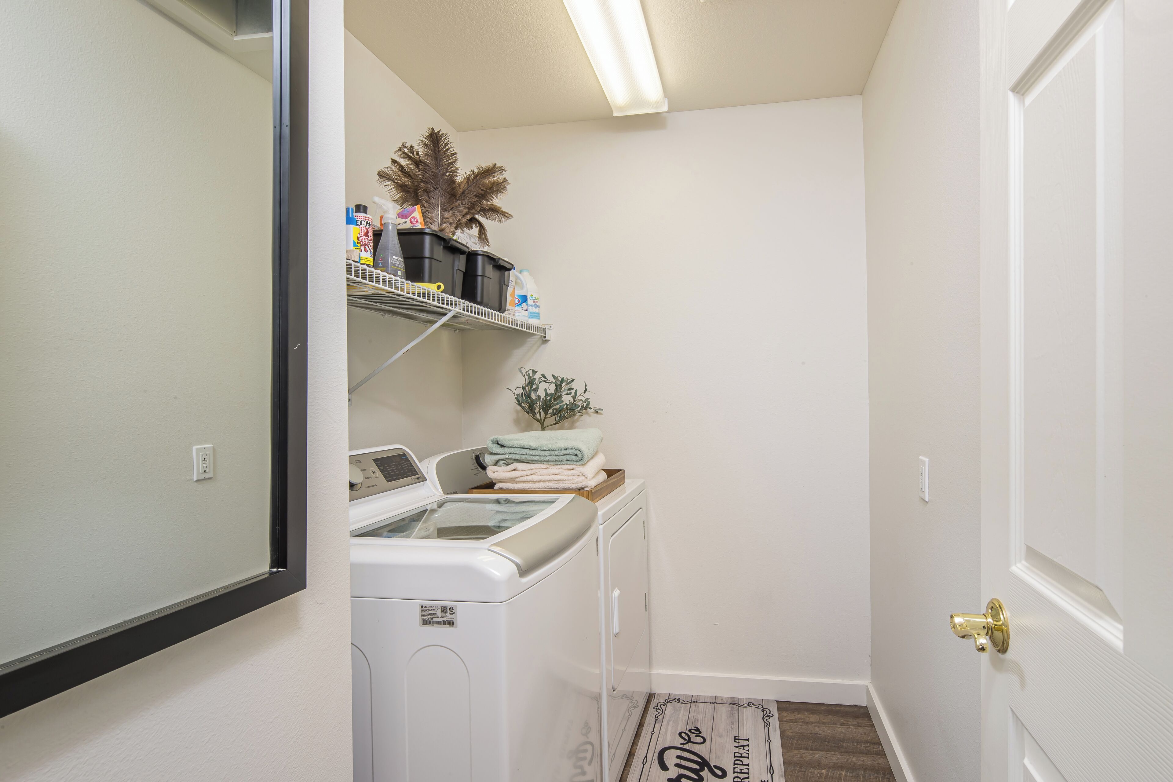A laundry room with a washing machine, dryer, shelves with cleaning supplies, and a door with a brass handle.