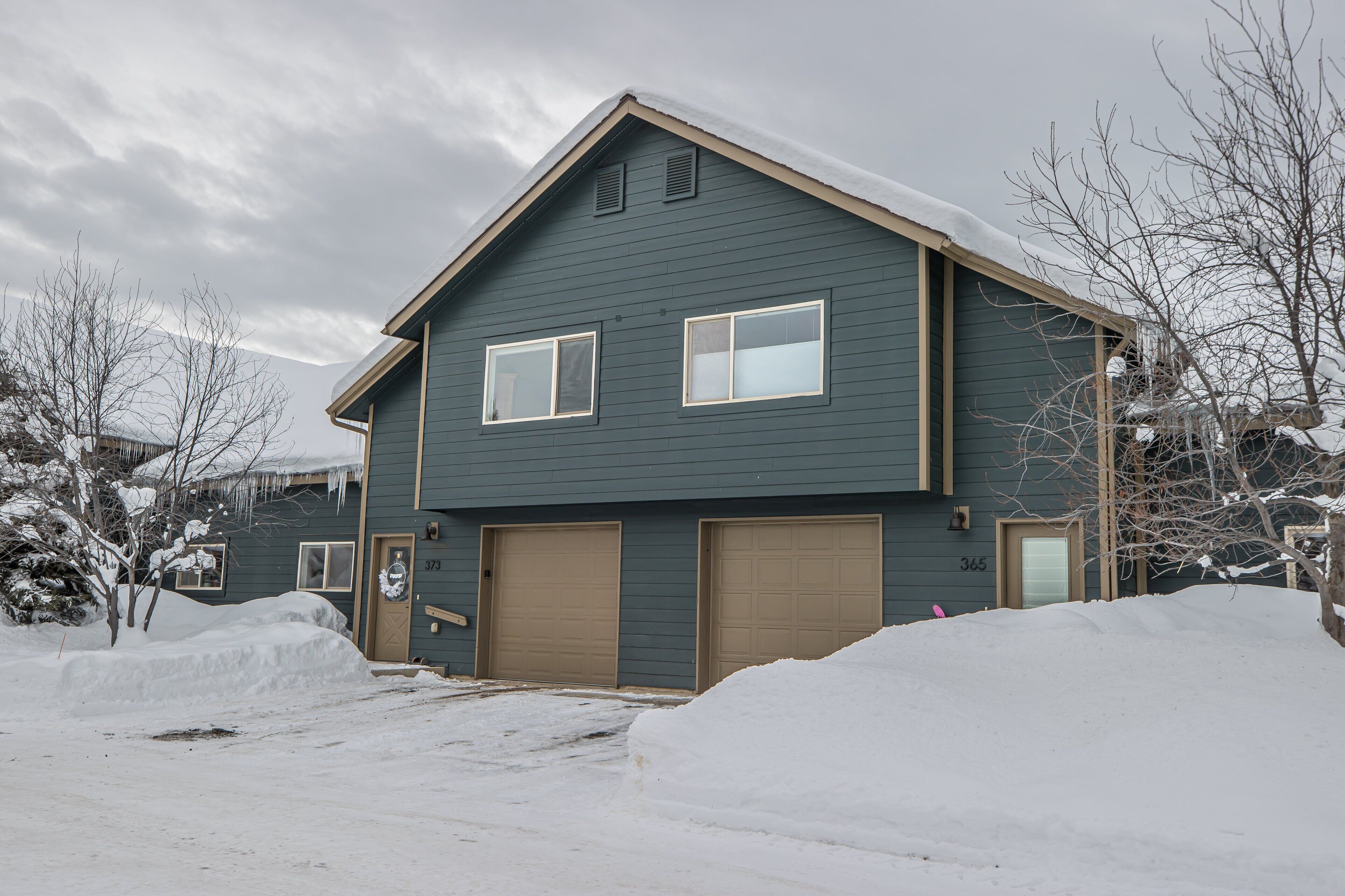 A two-story house with a dark blue exterior, two garage doors, and a snow-covered roof.