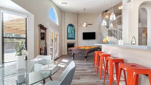 A modern living room with a pool table, orange bar stools, a glass coffee table, and a large window with blinds. - Paradise Palms House with Resort-Style Backyard, Pool and Hot Tub (Scottsdale)