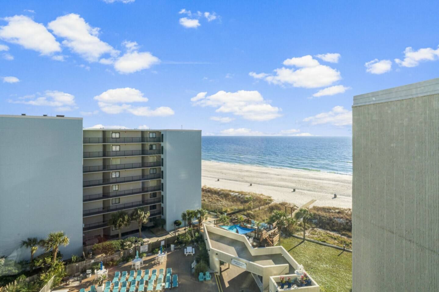 Un hotel con vista al mar, varios pisos y un área de piscina con sillones de descanso.