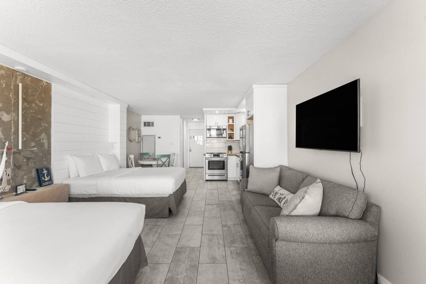 Un hotel moderno y luminoso con una cama grande, un sofá, un televisor montado en la pared y una kitchenette al fondo.