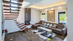 A modern living room with a wooden staircase, a sectional sofa, a fireplace, and large windows. - Beautiful villa Tamaria with heated pool and roof terrace (Zaton)