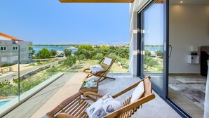 A balcony with two wooden lounge chairs, a small table with a cup and a book, and a glass door leading to a room. - Beautiful villa Tamaria with heated pool and roof terrace (Zaton)