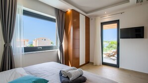 A modern hotel room with a large bed, a TV mounted on the wall, and a sliding glass door leading to a balcony with a view of buildings and greenery. - Beautiful villa Tamaria with heated pool and roof terrace (Zaton)
