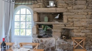 Comedor con suelo de piedra, pared de piedra rústica, sillas de madera, mesa dispuesta para dos y una lámpara colgante.