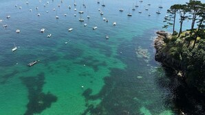 A coastal area with numerous boats anchored in clear blue waters, surrounded by rocky terrain and sparse vegetation.